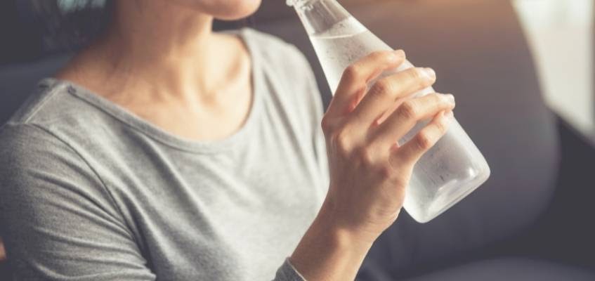 Холодная вода мешает пищеварению Девушка пьет из бутылки холодную воду